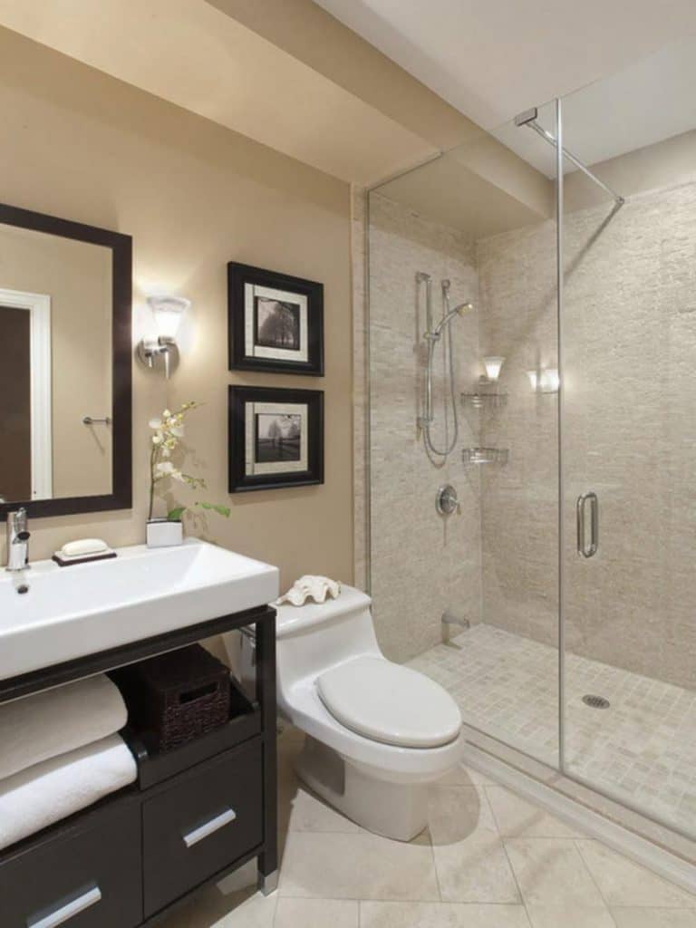 Phòng tắm nhỏ có thiết kế đơn giản, có buồng tắm kính và tủ gỗ dưới bồn rửa.